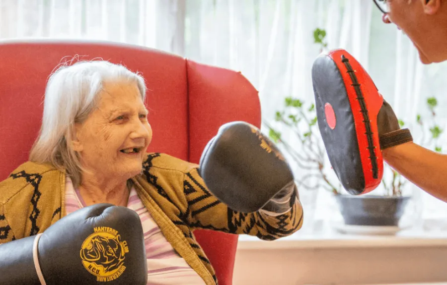 Lady in care home getting physical exercise with boxing - Maven Healthcare