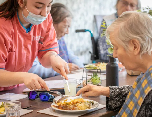 A nurse assisting a disabled resident with cutting up food - Maven Healthcare