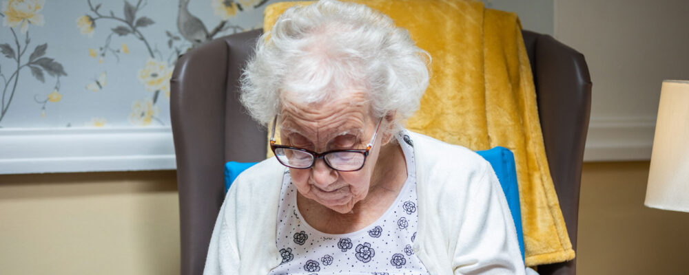 An elderly resident knitting in a comfy chair at St Oswalds House care home - Maven Healthcare